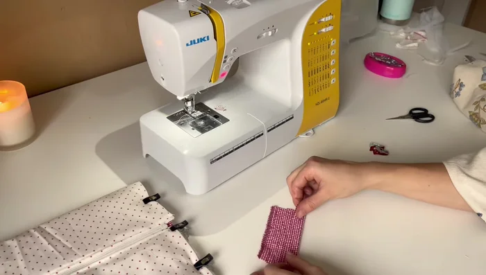 Prepare and attach the decorative fabric strip. Fold the edges of the small fabric square to the middle twice to create bias binding. Place it inside the pouch, centered on the zipper stop, and sew it in place. 