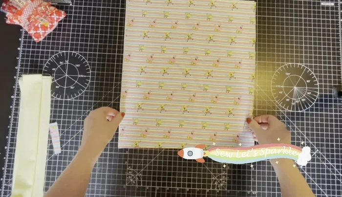 Attach Tabs to Outer Fabric: Fold the tabs in half. Measuring one inch from the bottom of your outer fabric, place the tabs, one on each side, and baste in place using a long stitch.