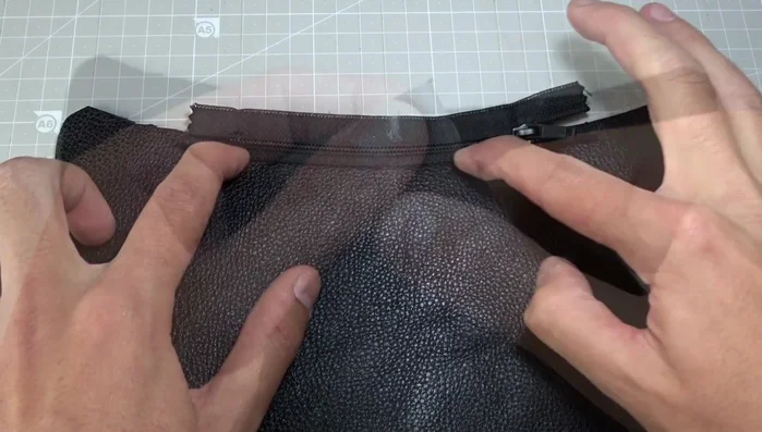 Mark the beginning and end of the seam with chalk, ensuring the zipper is open halfway before sewing. Sew the zipper to the second leather piece. Repeat the step of lowering the needle and opening the zipper halfway to sew around the zipper.