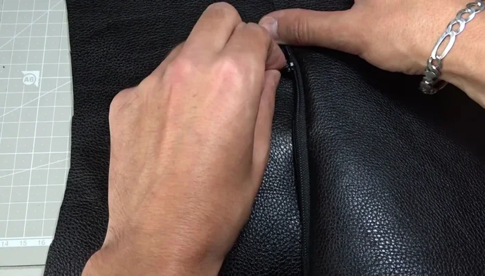 Mark the beginning and end of the seam with chalk, ensuring the zipper is open halfway before sewing. Sew the zipper to the second leather piece. Repeat the step of lowering the needle and opening the zipper halfway to sew around the zipper.