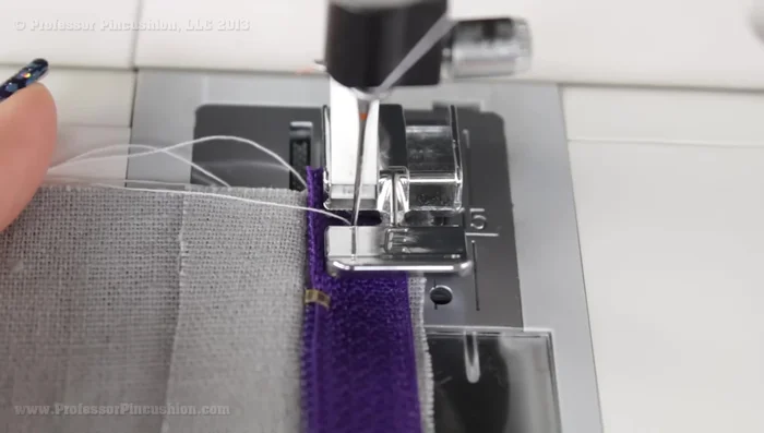 Baste the zipper tape to the fabric using a zipper foot on your machine. Use a basting stitch. To avoid sewing over the zipper pull, temporarily lift the presser foot, zip up past the pull, then continue sewing.
