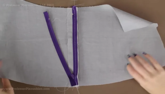 Using a matching thread and a regular stitch, stitch along the basting stitches to permanently secure the zipper tape. Aim for about a quarter-inch away from the zipper teeth.