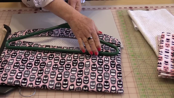 Create a pattern. Trace the hanger's shape three times, adding a ¼ inch seam allowance. Add a 2-inch space at the top for hanger insertion and a 10-inch square at the bottom for the pocket. Curve the top and bottom lines to create the pocket opening.