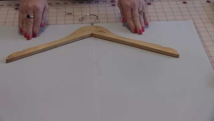 Create a pattern. Trace the hanger's shape three times, adding a ¼ inch seam allowance. Add a 2-inch space at the top for hanger insertion and a 10-inch square at the bottom for the pocket. Curve the top and bottom lines to create the pocket opening.