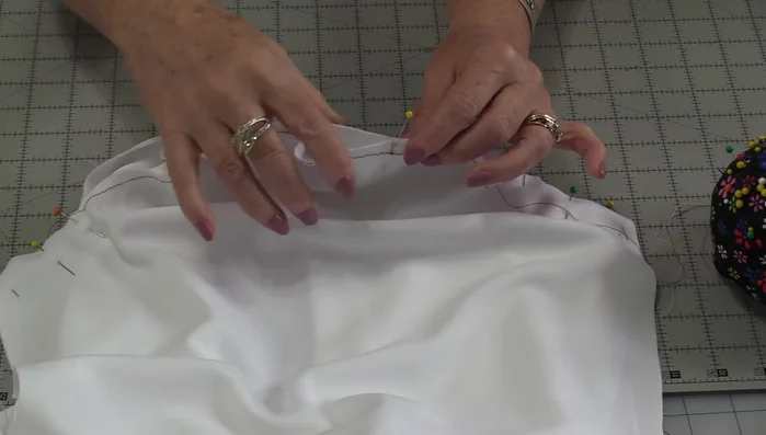 Ease and distribute fabric: Gently pull basting threads to ease the sleeve's fullness, ensuring even distribution of fabric between pins. Work in sections to maintain an even fit.