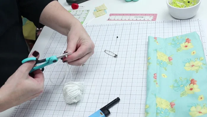 Insert Drawstring: Cut two 19-20" lengths of drawstring material (cord, twine, ribbon). Seal the ends with a lighter if needed. Attach a safety pin to one end of each drawstring. Insert each drawstring through the channel. Tie off the ends.