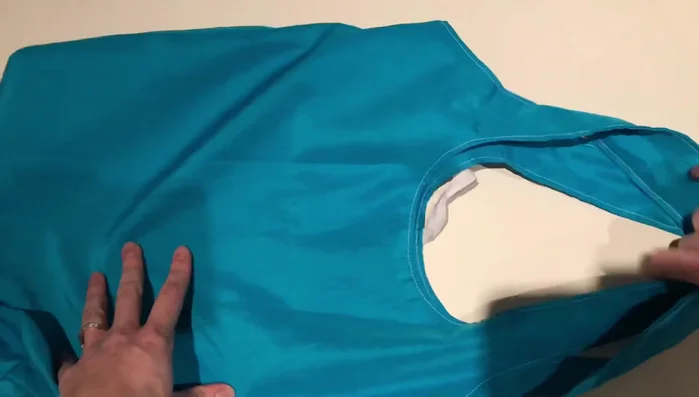 Fold the bag into thirds, tucking in the straps and bottom. Roll it up tightly and tuck the elastic over the top.