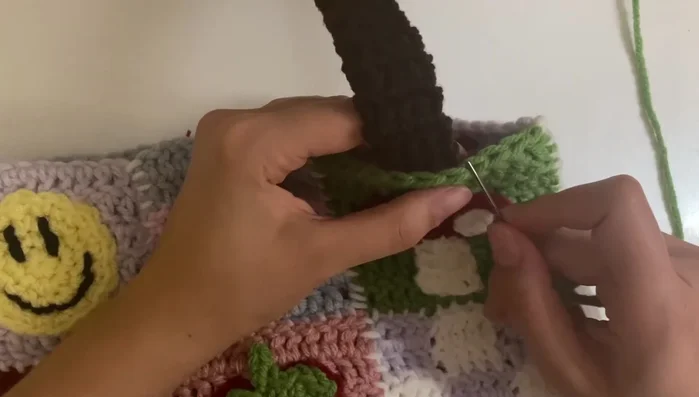 Attach handles by securing them to the bag with yarn matching the bag's background. Ensure even spacing and sturdiness.