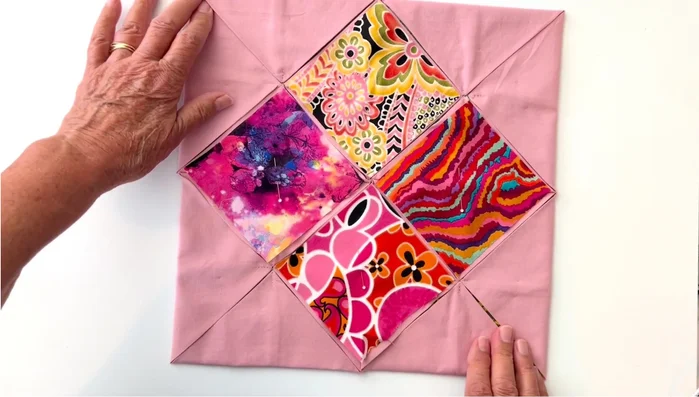 Machine Sew the Windows: Using an edge stitch foot, top stitch along the diagonal lines, securing the points at the start and end of each seam. Needle down, lift the presser foot, remove pins, adjust fabric, and continue stitching along each line, revealing the inner windows as you go.