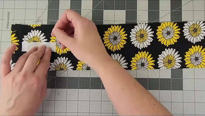 Sew Velcro to the fabric side of the fused piece. Pin a piece of Velcro about half an inch from each end of the fabric and sew in place.