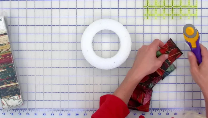 Prepare Jingle Pop Strips: Trim the selvage from the 2.5-inch Jingle Pop strips. Lay a strip around the wreath and secure it with pins.