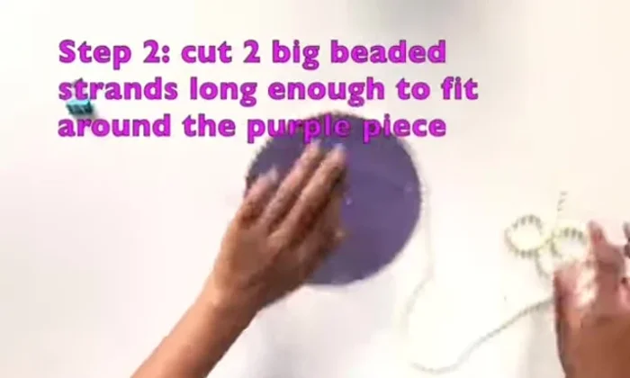 Turn the purple piece over and thread the big beaded strands through the holes across from each other in the center, then feed the strands through the outside holes. Repeat with the second strand.