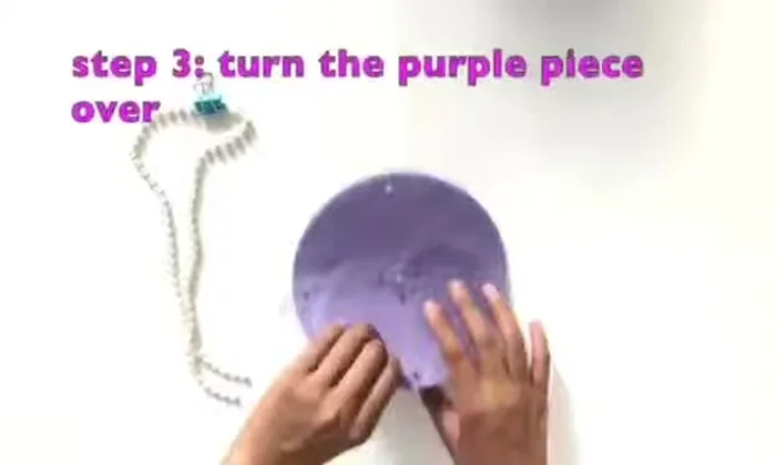Turn the purple piece over and thread the big beaded strands through the holes across from each other in the center, then feed the strands through the outside holes. Repeat with the second strand.