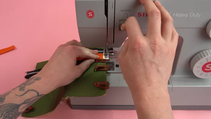 Cut two six-inch strips of one-inch webbing and sew them under the zipper edge.