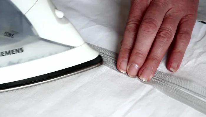 Press the rolled edge of the zipper flat with an iron.