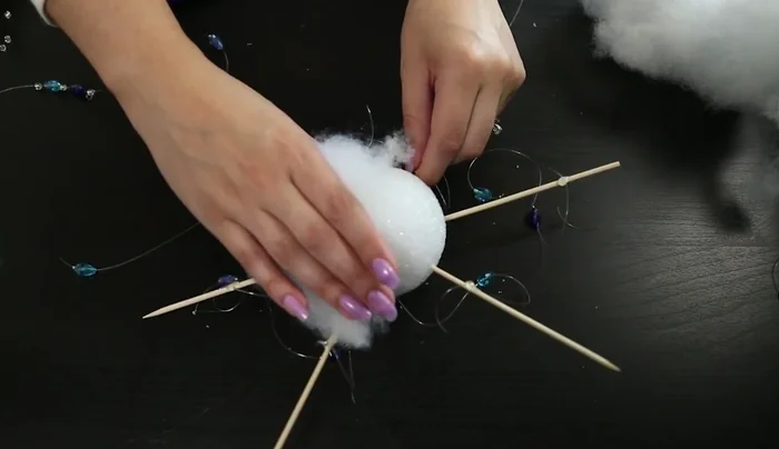 Ensure the bead strings remain visible and not glued down. Continue adding glue and shaping the batting around the edges to complete the cloud shape.