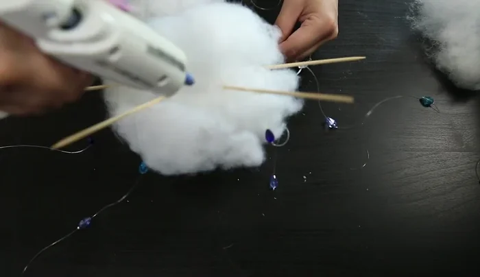 Ensure the bead strings remain visible and not glued down. Continue adding glue and shaping the batting around the edges to complete the cloud shape.