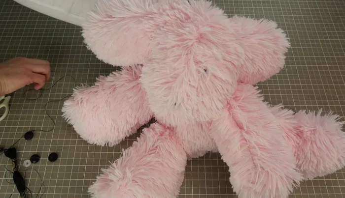 Attach eyes using a button and needle, securing with stitches that also sculpt the face by incorporating the stuffing.