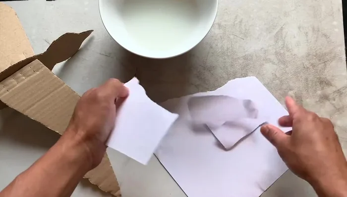 Tear printer paper into small pieces and apply them to both sides of the cardboard bird, overlapping pieces to avoid wrinkles and air bubbles. Do not papier-mâché the wing hinges. Allow several hours to dry, keeping the wings straight using containers.