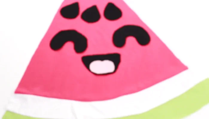 Attach the facial details. Use needles to attach the black fabric features to the watermelon. 