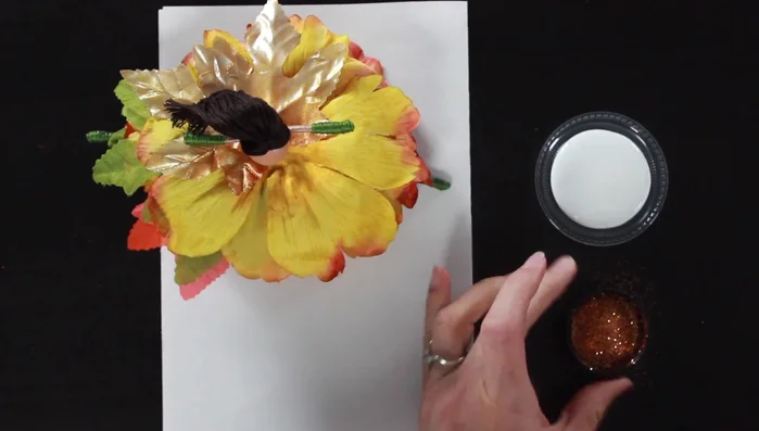 Add glitter. Apply Mod Podge around the doll's waist and sprinkle with bronze glitter. Dip the tips of some leaves in glue and gold glitter for extra sparkle.